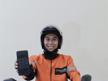 Rider pertama MyJek tersenyum di atas motor sambil menunjukkan ponsel